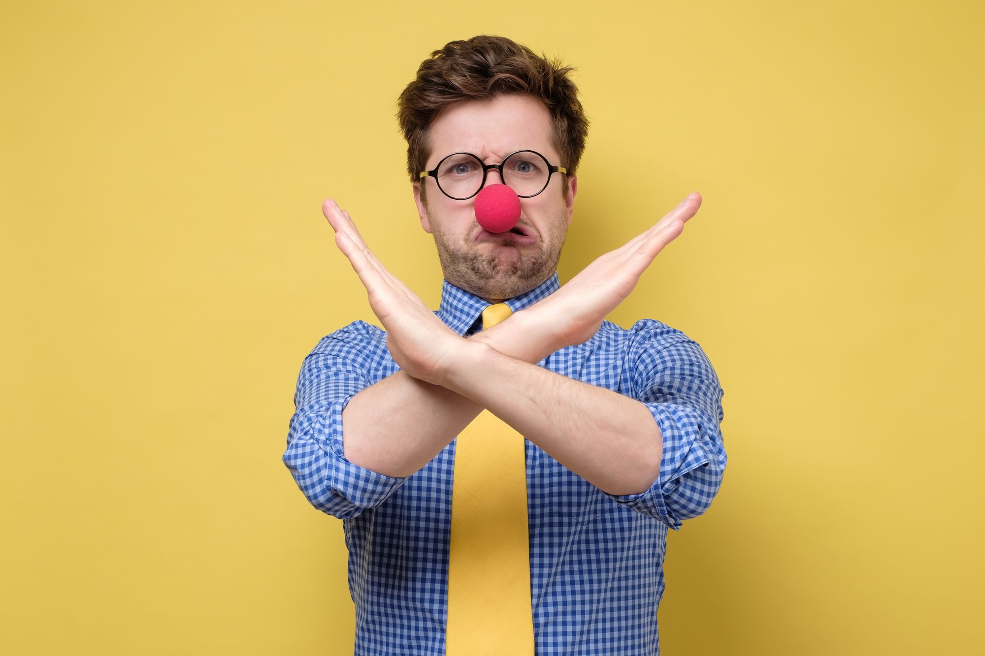 Funny caucasian man with red clown nose over isolated yellow background making stop gesture. First April concept