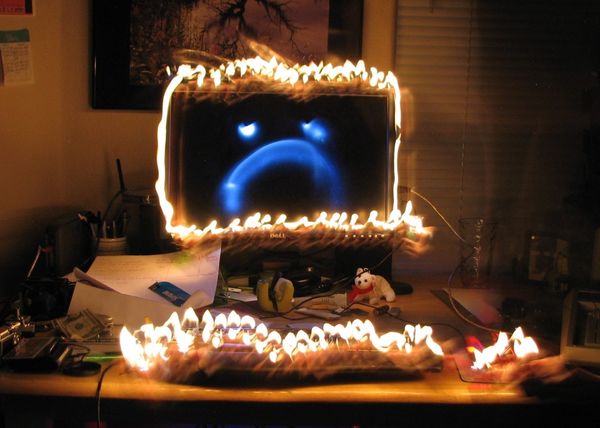 Blue sad face computer screen surrounded by burning candles. Candles are also on keyboard and mouse.